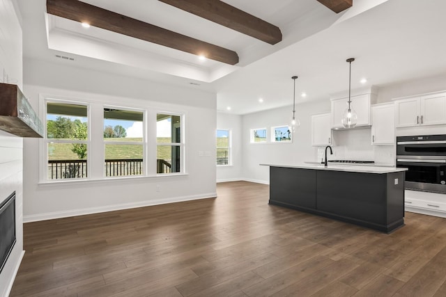 kitchen with pendant lighting, white cabinetry, double oven, an island with sink, and dark hardwood / wood-style flooring