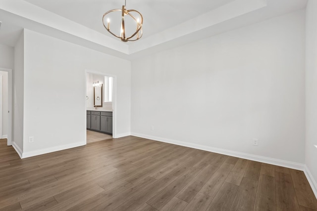 unfurnished room with a chandelier, dark hardwood / wood-style flooring, and a raised ceiling