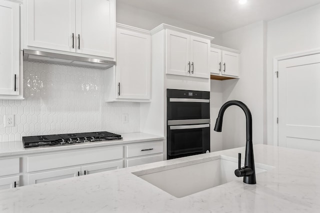 kitchen featuring white cabinetry, black double oven, light stone countertops, and stainless steel gas cooktop