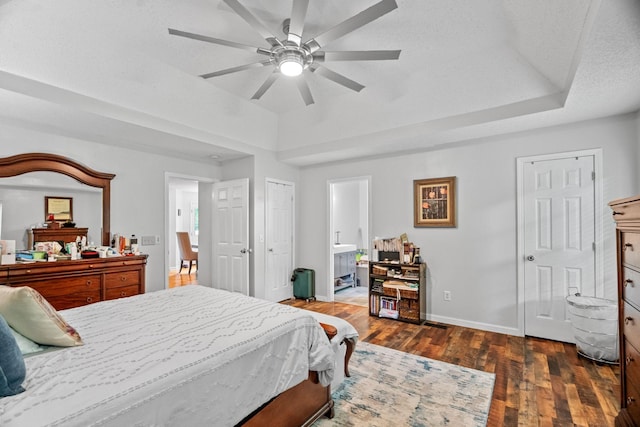 bedroom with a tray ceiling, dark hardwood / wood-style floors, ceiling fan, and ensuite bathroom