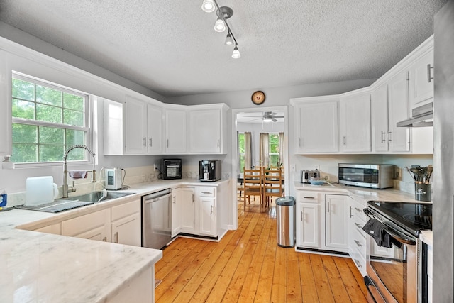 kitchen with appliances with stainless steel finishes, sink, white cabinets, light hardwood / wood-style floors, and plenty of natural light