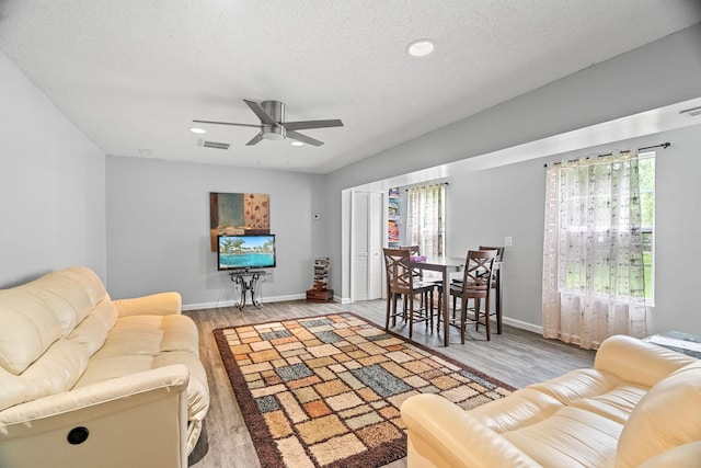 living room featuring ceiling fan, light hardwood / wood-style flooring, and a textured ceiling