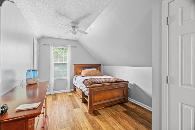 bedroom featuring lofted ceiling, ceiling fan, light hardwood / wood-style floors, and a textured ceiling