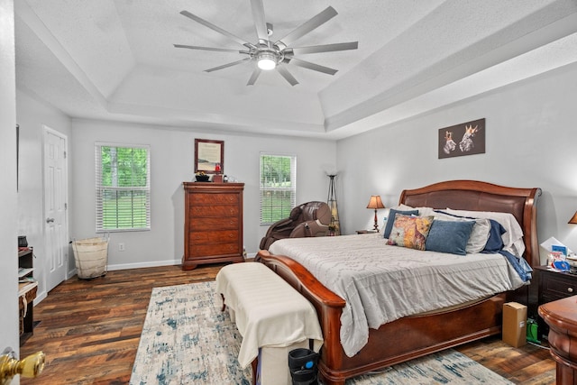 bedroom with dark hardwood / wood-style flooring, a raised ceiling, multiple windows, and a textured ceiling