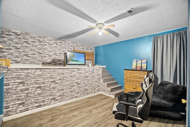 sitting room with hardwood / wood-style flooring, a textured ceiling, ceiling fan, and brick wall