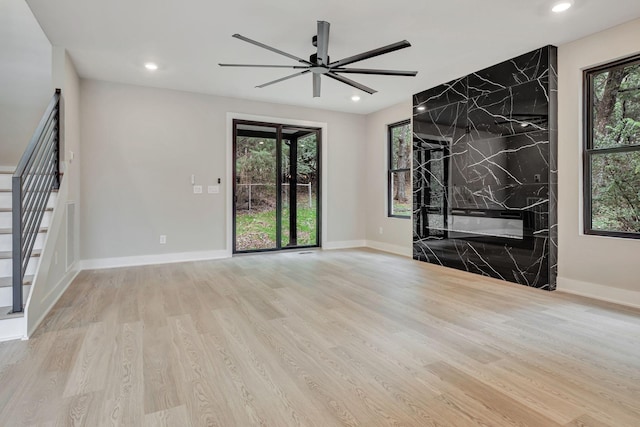 unfurnished living room featuring ceiling fan, a fireplace, light hardwood / wood-style floors, and a wealth of natural light