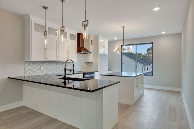 kitchen with a kitchen island, sink, white cabinets, hanging light fixtures, and wall chimney exhaust hood