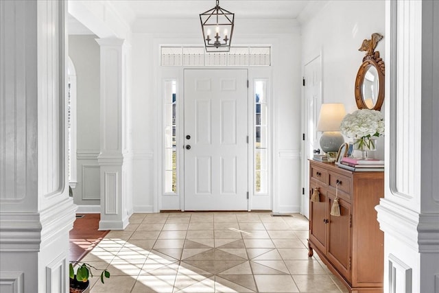 entrance foyer with ornate columns, ornamental molding, light tile patterned floors, and an inviting chandelier