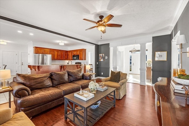 living room featuring crown molding, a textured ceiling, dark hardwood / wood-style floors, ceiling fan, and decorative columns