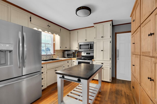 kitchen with sink, dark wood-type flooring, appliances with stainless steel finishes, ornamental molding, and cream cabinetry