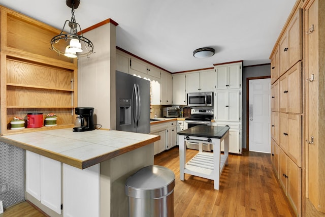 kitchen featuring appliances with stainless steel finishes, tile countertops, pendant lighting, kitchen peninsula, and light hardwood / wood-style flooring