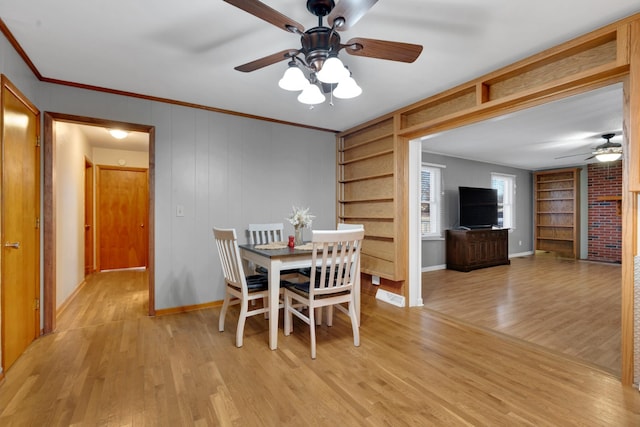 dining space featuring built in features, ornamental molding, ceiling fan, and light wood-type flooring