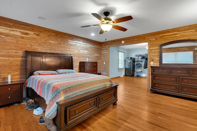 bedroom featuring ceiling fan, wooden walls, and light hardwood / wood-style flooring