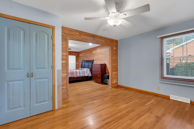 unfurnished bedroom with ceiling fan, wooden walls, light hardwood / wood-style floors, and a closet