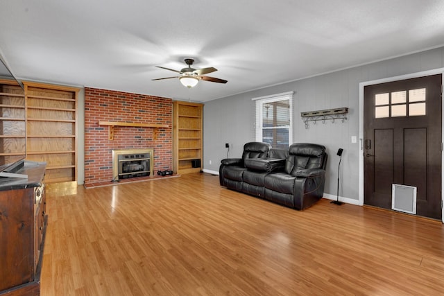 living room with a brick fireplace, built in shelves, light hardwood / wood-style flooring, and ceiling fan