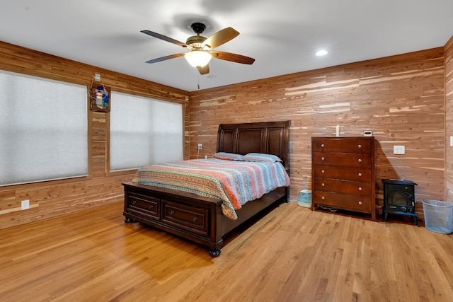 bedroom with ceiling fan, a wood stove, light hardwood / wood-style floors, and wood walls