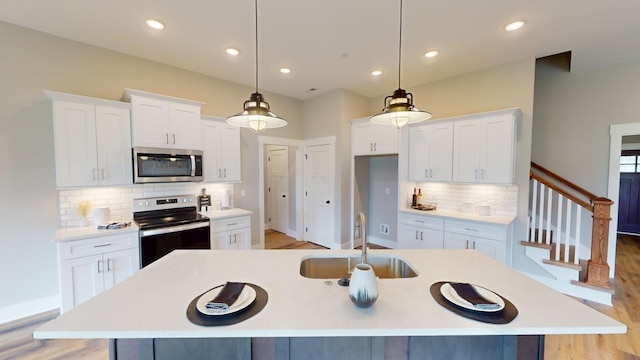 kitchen featuring white cabinetry, decorative light fixtures, an island with sink, and appliances with stainless steel finishes