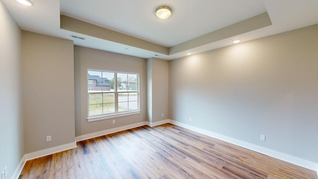 spare room featuring light hardwood / wood-style floors and a raised ceiling