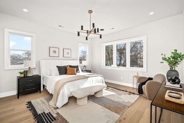 bedroom featuring multiple windows, an inviting chandelier, and light hardwood / wood-style flooring