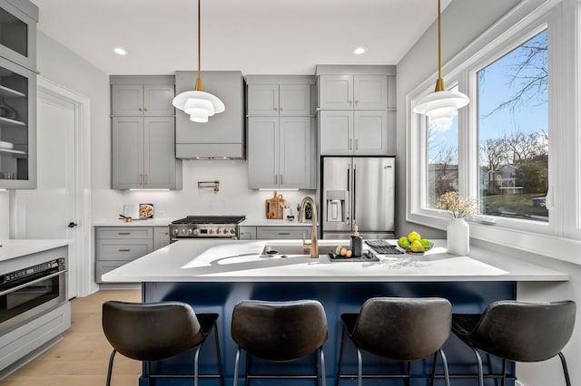 kitchen with gray cabinetry, light wood-type flooring, a kitchen breakfast bar, and appliances with stainless steel finishes