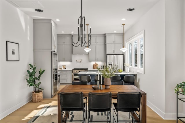 kitchen with gray cabinetry, a chandelier, light hardwood / wood-style flooring, hanging light fixtures, and appliances with stainless steel finishes