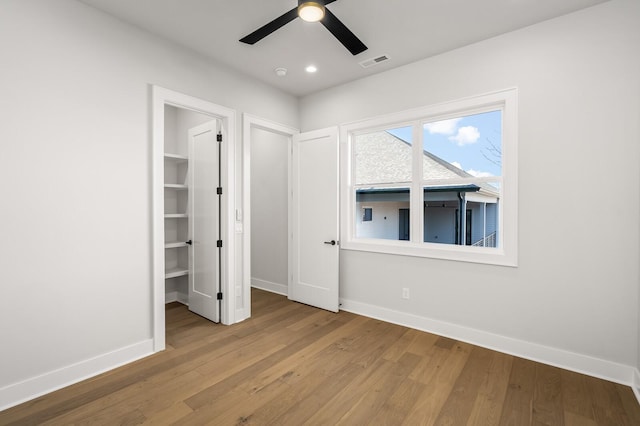 unfurnished bedroom featuring ceiling fan, a walk in closet, light hardwood / wood-style floors, and a closet