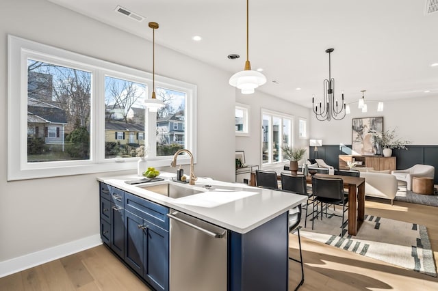 kitchen featuring pendant lighting, blue cabinets, dishwasher, sink, and a kitchen breakfast bar