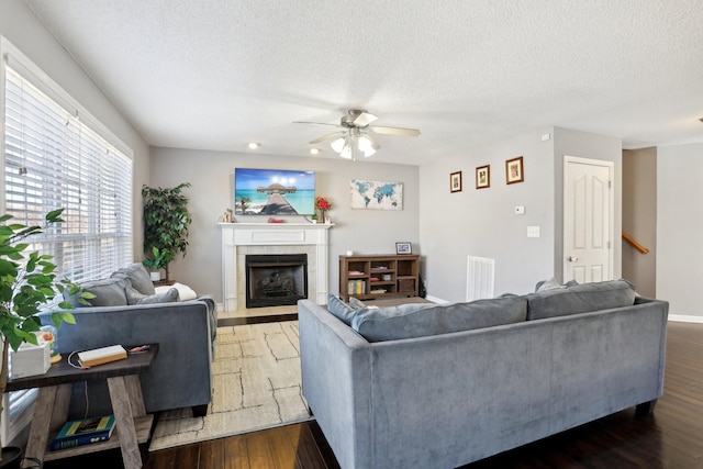 living room featuring ceiling fan, a fireplace, dark hardwood / wood-style flooring, and a textured ceiling