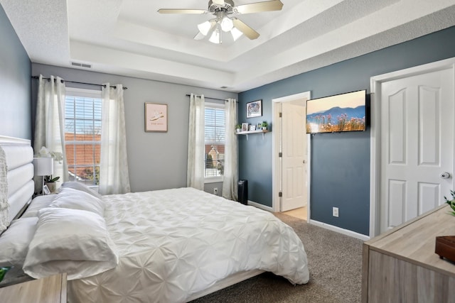 carpeted bedroom featuring multiple windows, a raised ceiling, and ceiling fan