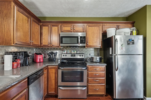 kitchen with dark hardwood / wood-style floors, dark stone countertops, backsplash, stainless steel appliances, and a textured ceiling