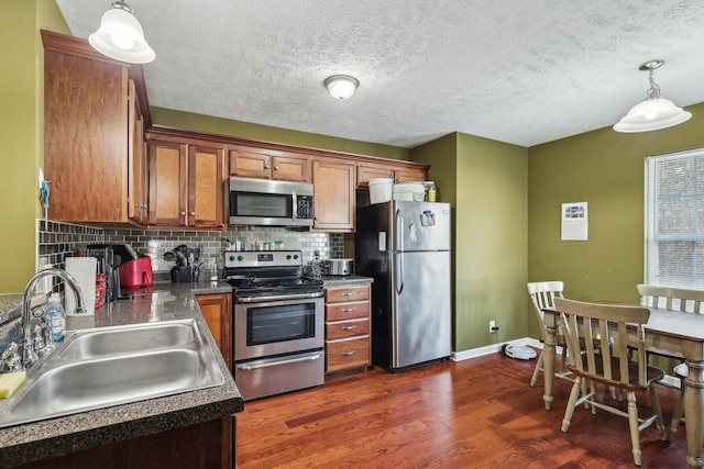 kitchen with sink, appliances with stainless steel finishes, hanging light fixtures, backsplash, and dark hardwood / wood-style flooring