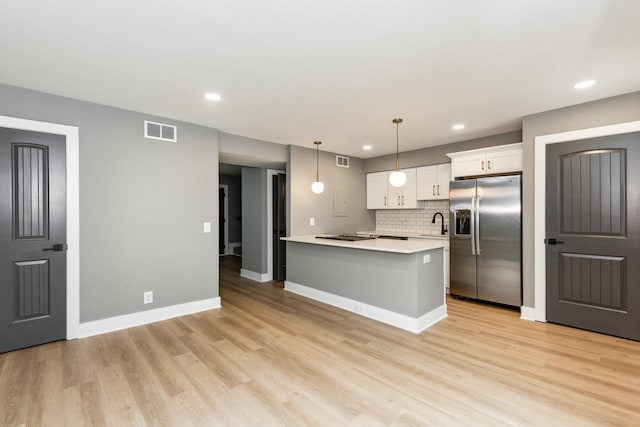 kitchen with pendant lighting, stainless steel fridge, light hardwood / wood-style floors, an island with sink, and white cabinets