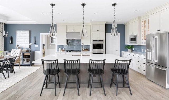 kitchen with pendant lighting, stainless steel appliances, sink, and a kitchen island with sink