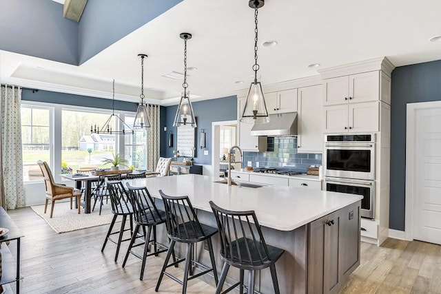 kitchen with double oven, decorative light fixtures, sink, white cabinets, and a large island