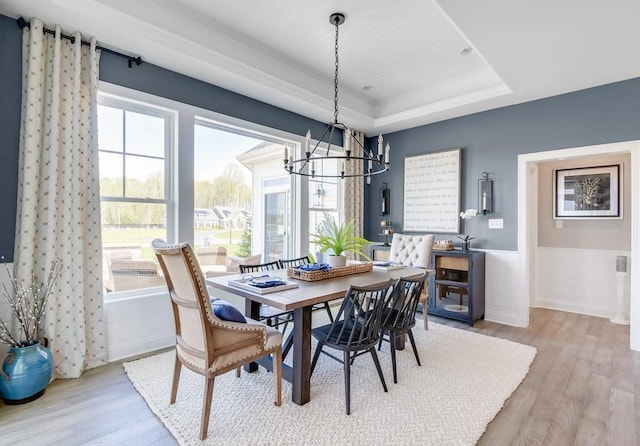 dining room featuring a raised ceiling, a chandelier, and light wood-type flooring