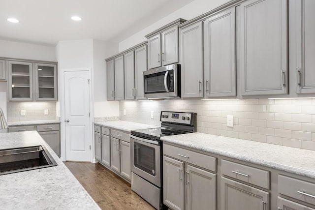 kitchen featuring light stone countertops, gray cabinets, stainless steel appliances, and light wood-type flooring