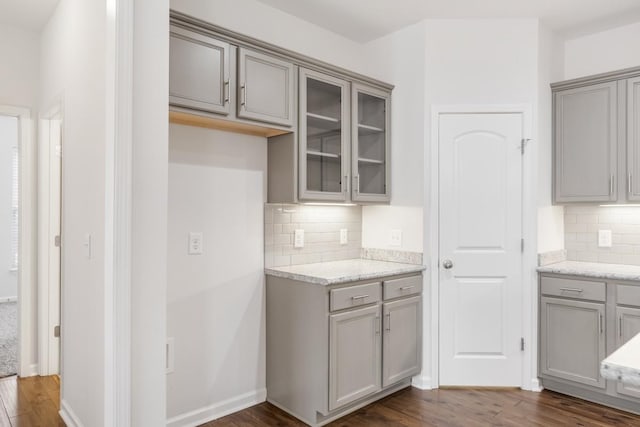 kitchen with gray cabinetry, decorative backsplash, dark wood-type flooring, and light stone countertops