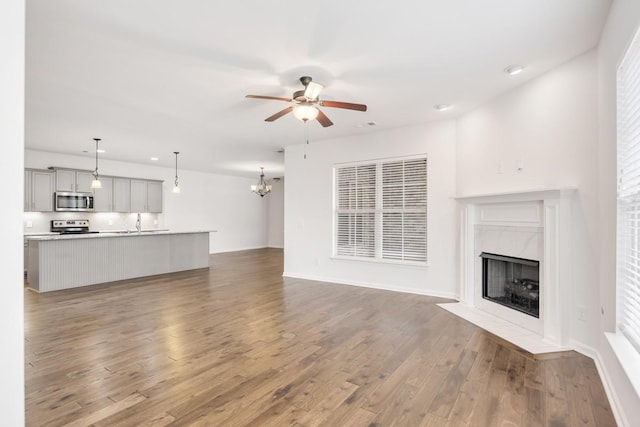 unfurnished living room with hardwood / wood-style floors, ceiling fan with notable chandelier, and a high end fireplace