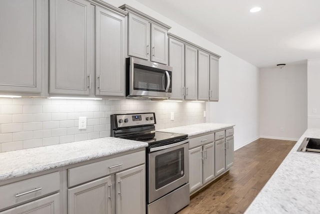 kitchen featuring hardwood / wood-style flooring, stainless steel appliances, gray cabinets, and tasteful backsplash