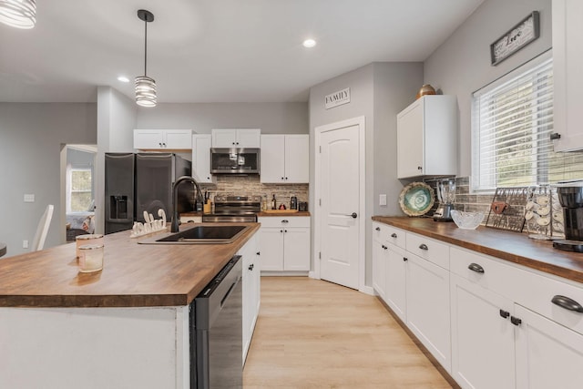 kitchen with pendant lighting, wood counters, appliances with stainless steel finishes, and a kitchen island with sink