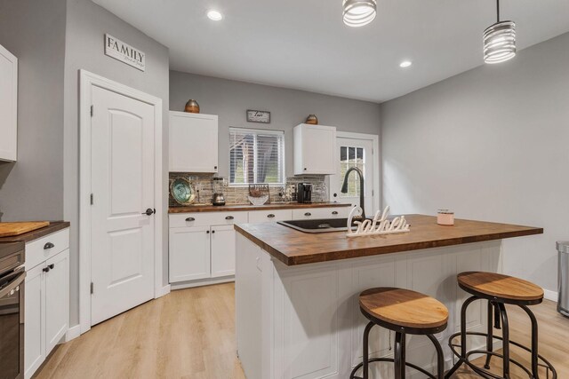 kitchen with a breakfast bar area, wooden counters, white cabinets, a center island with sink, and decorative light fixtures