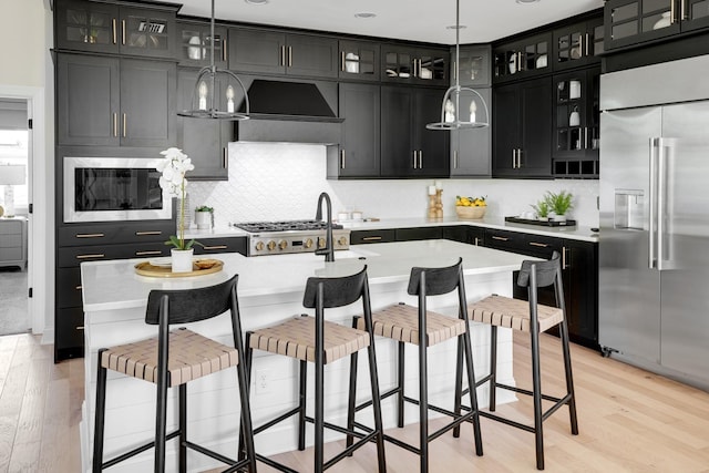 kitchen featuring built in appliances, decorative light fixtures, a breakfast bar, and a center island with sink