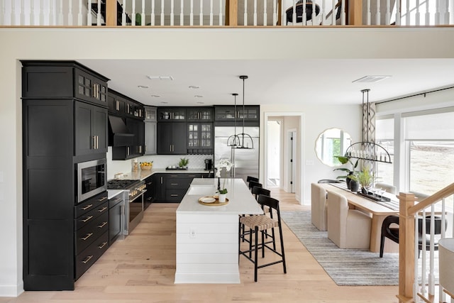 kitchen featuring wall chimney range hood, a breakfast bar area, built in appliances, an island with sink, and a chandelier