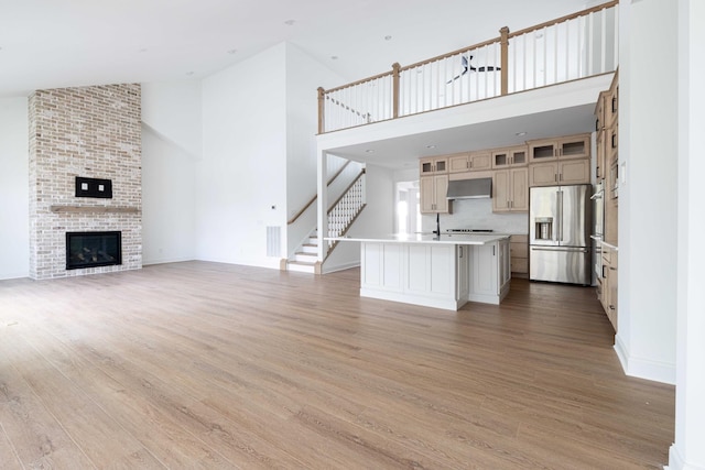 unfurnished living room featuring a brick fireplace, high vaulted ceiling, and light hardwood / wood-style flooring