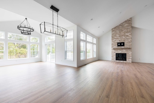 unfurnished living room with high vaulted ceiling, a brick fireplace, hardwood / wood-style floors, and a chandelier