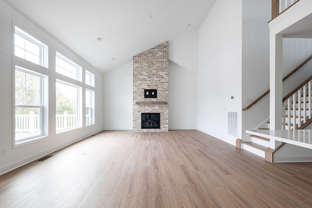 unfurnished living room featuring wood-type flooring, a brick fireplace, and high vaulted ceiling