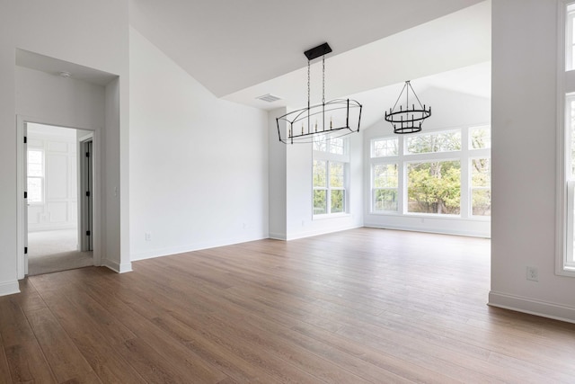 unfurnished dining area with wood-type flooring, vaulted ceiling, and a chandelier