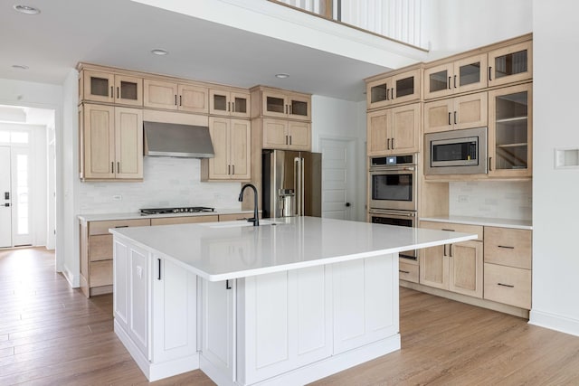 kitchen featuring a kitchen island with sink, wall chimney range hood, stainless steel appliances, and sink