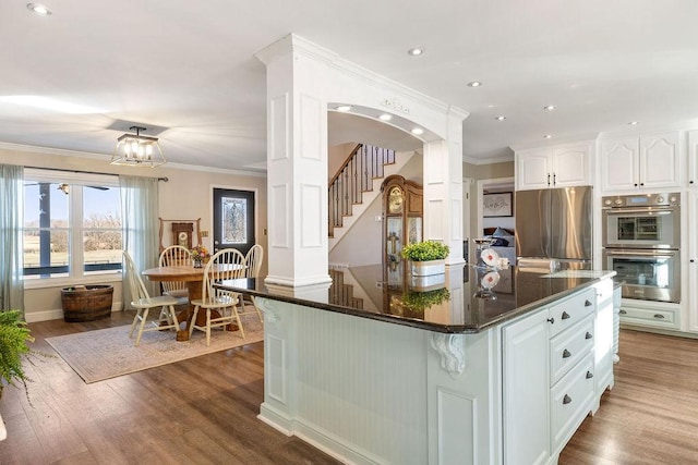 kitchen with crown molding, a center island, appliances with stainless steel finishes, hardwood / wood-style floors, and white cabinets