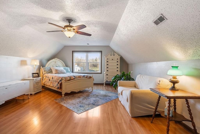 bedroom with vaulted ceiling, a textured ceiling, and light wood-type flooring